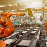 Rows of orange industrial robot arms on an automated factory assembly floor